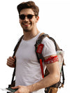 Smiling man wearing a white t-shirt and sunglasses, with a backpack that has a red 'Medical Supply Bag Handle With Care' luggage tag attached.