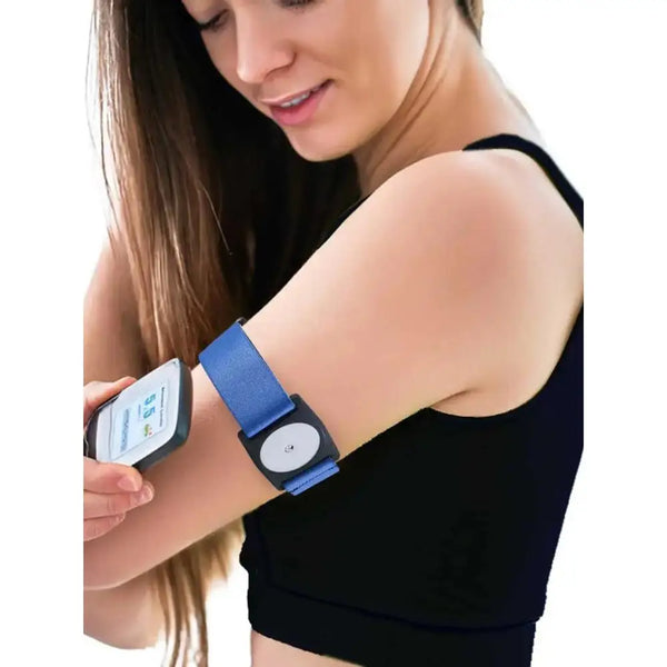 A woman using a smartphone app while wearing a Freestyle Libre 2 Armband on her upper arm. The armband is blue and securely holds the sensor.