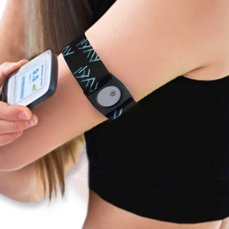 Person wearing a Freestyle Libre 3 armband on their upper arm, holding the glucose monitor to check levels. The black armband with blue patterns provides a snug fit for sports and activities. Image