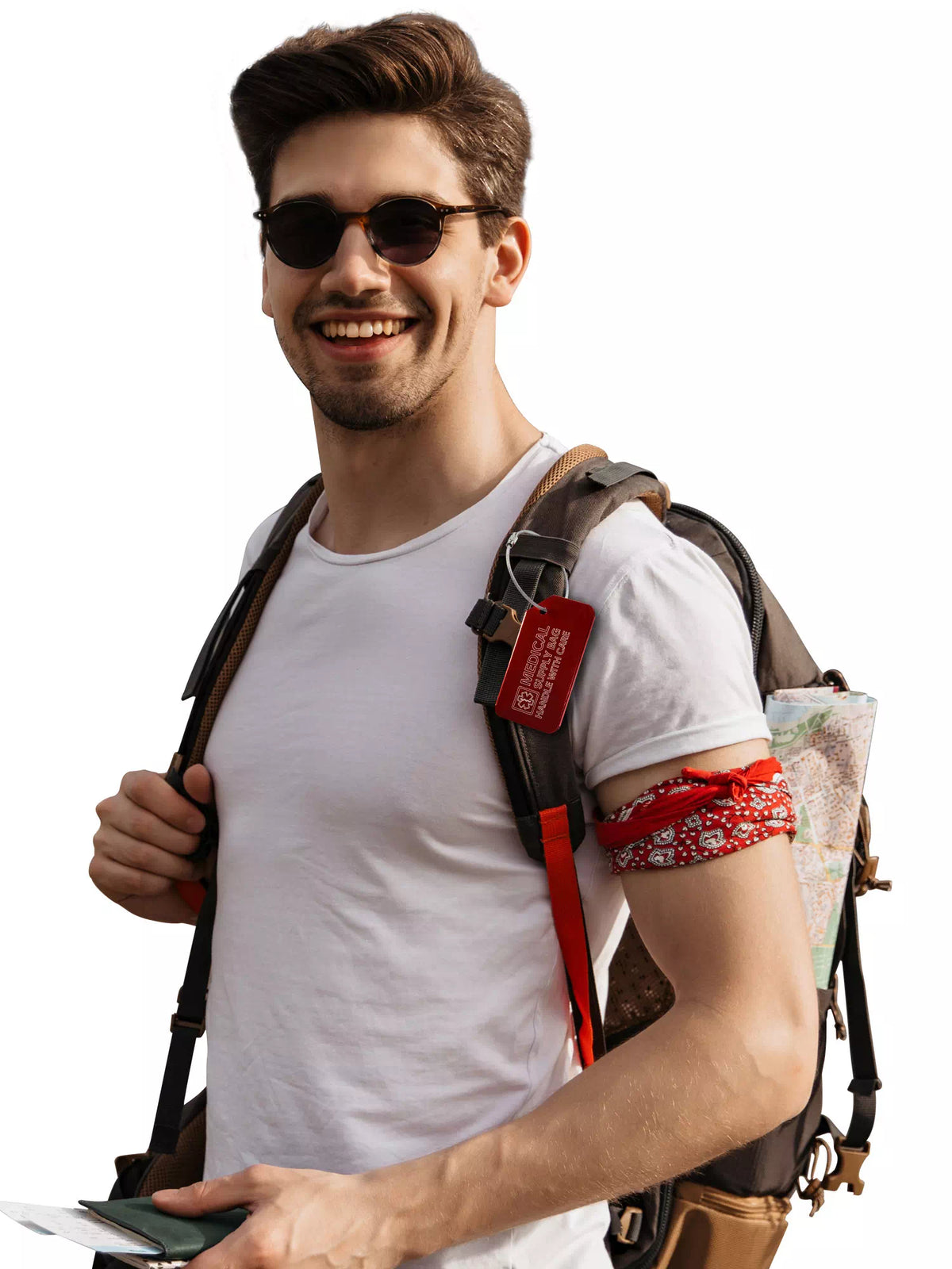 Smiling man wearing a white t-shirt and sunglasses, with a backpack that has a red 'Medical Supply Bag Handle With Care' luggage tag attached.