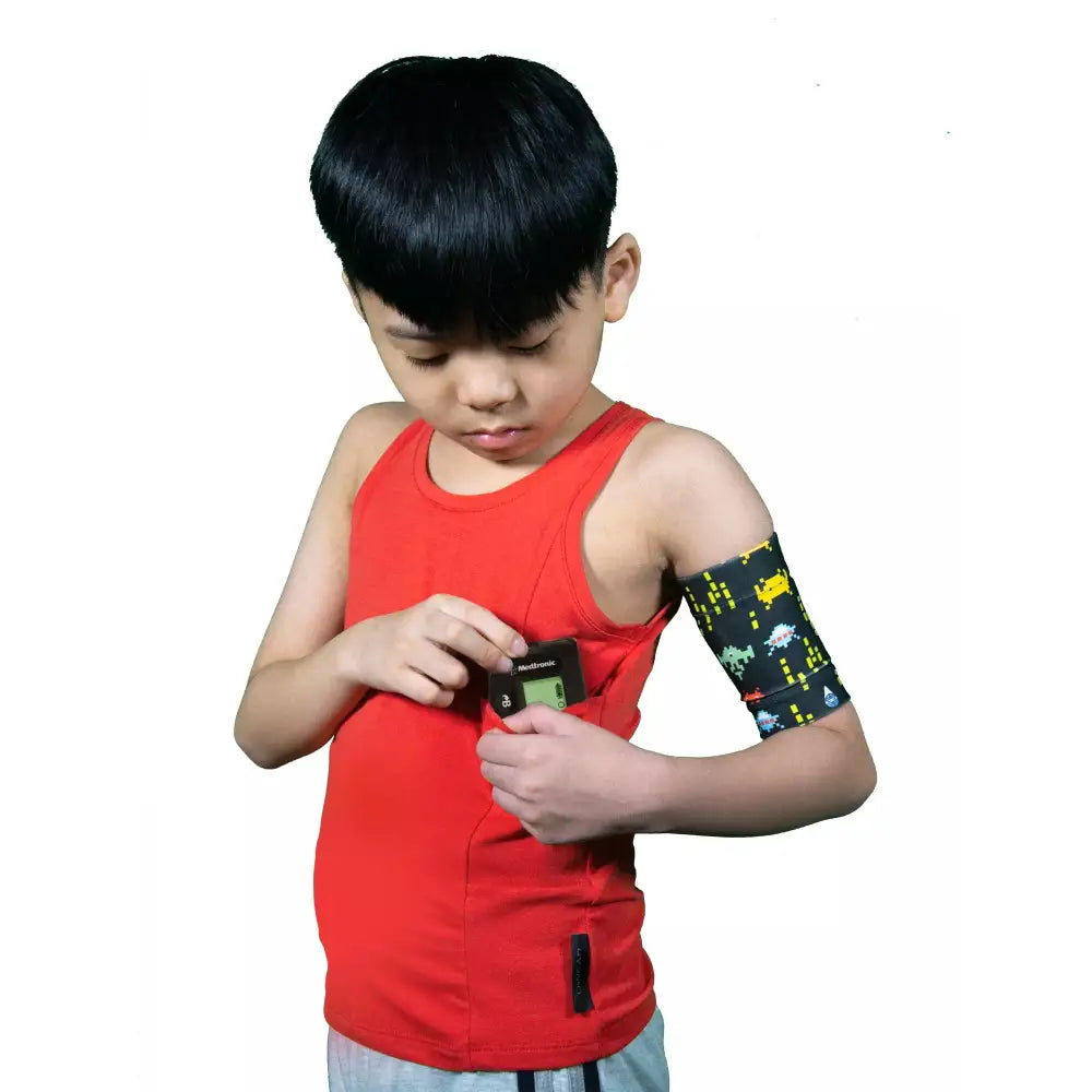 Child wearing red tank top with insulin pump pocket; designed for comfort and daily activities.